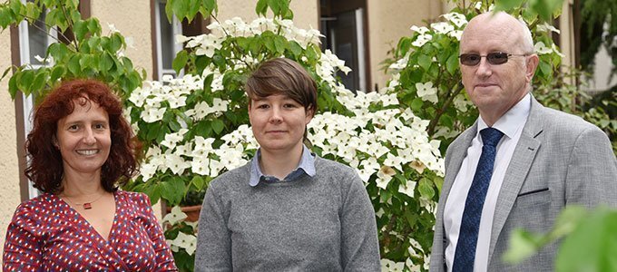 Auf dem Bild stehen links Dorothee Gößner (Koordinatorin), in der Mitte Ariane Kehr (konzeptionelle Mitarbeit) und rechts Prof. Dr. David J. Green (Diversitätsbeauftragter) vor einem weiß-blühendem Strauch.
