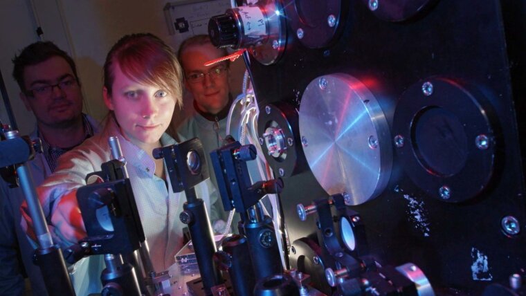 Two male researchers and a female researcher at a large device in a physics lab