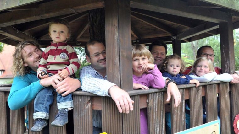 Four children and their fathers laughing in a children's house on a playground.
