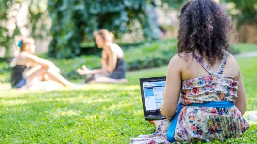 Studentin sitz auf einer grünen Wiese und arbeitet am Laptop