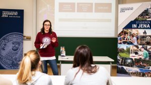 Eine junge Frau berichtet einem Publikum von der Uni Jena, links und rechts stehen Roll-ups