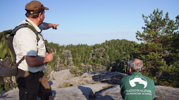 Ein Ranger des Nationalparks Sächsische Schweiz zeigt auf eine Waldfläche mit illegaler Feuerstelle.