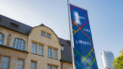 A flag with the slogan "Light. Life. Liberty" in front of the main university building