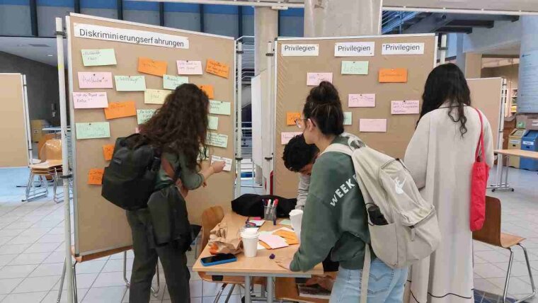 Studierende kleben Zettel mit Diversitätsinformation auf Stellwände