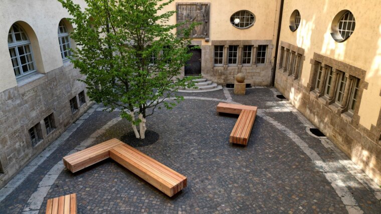 Kleiner Innenhof de Universitätshauptgebäudes mit drei Bänken und einem Baum