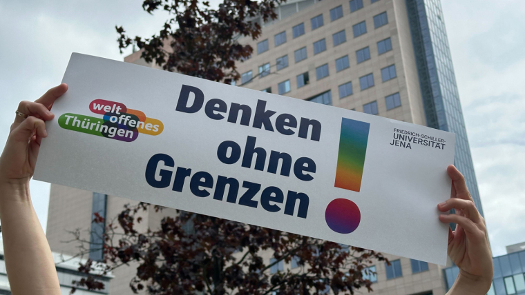 Two hands hold up a banner with the German words for "Thinking without borders".