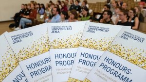 Flyer und Publikum zur feierlichen Begrüßung der Honours-Studierenden 2024 in der Aula im Universitätshauptgebäude