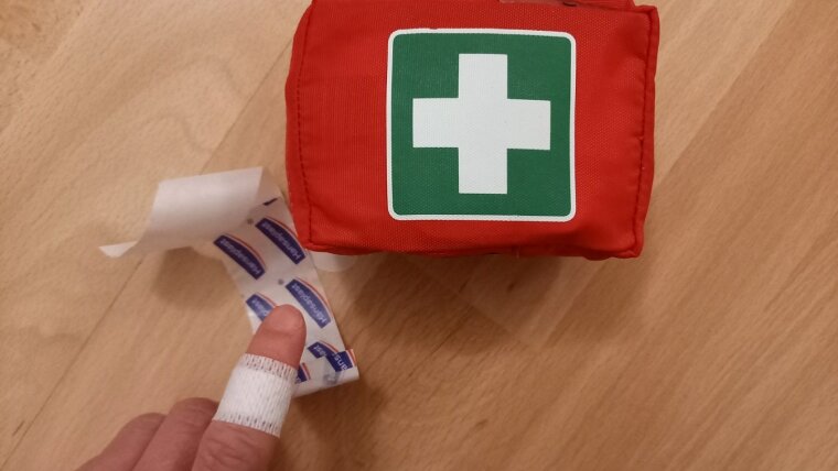 Erste-Hilfe-Tasche und Finger mit Pflaster