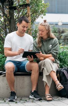 Zwei Studierende sitzen und arbeiten mit einem Tablet