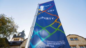 Eine Fahne mit dem Slogan "Light, Life, Liberty" vor dem Hauptgebäude der Friedrich-Schiller-Universität Jena