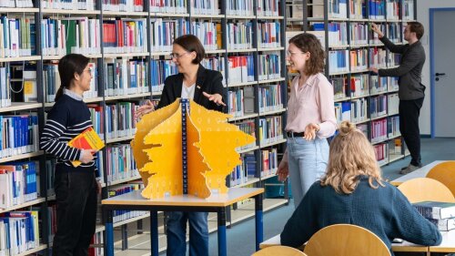 Wirtschaftswissenschaftlerinnen diskutieren vor einem Modell der Bevölkerungspyramide.