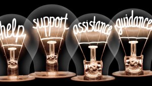 Auf schwarzem Grund leuchten vier Glühbirnen, deren Drähte jeweils eines der Worte "help, support, assistance, guidance" formen